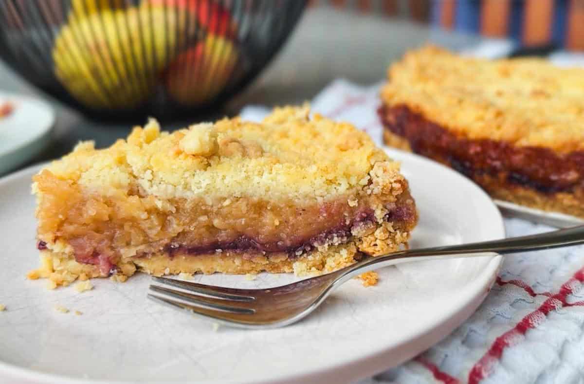 Close-up of a slice of fruit pie with crumble topping on a white plate.