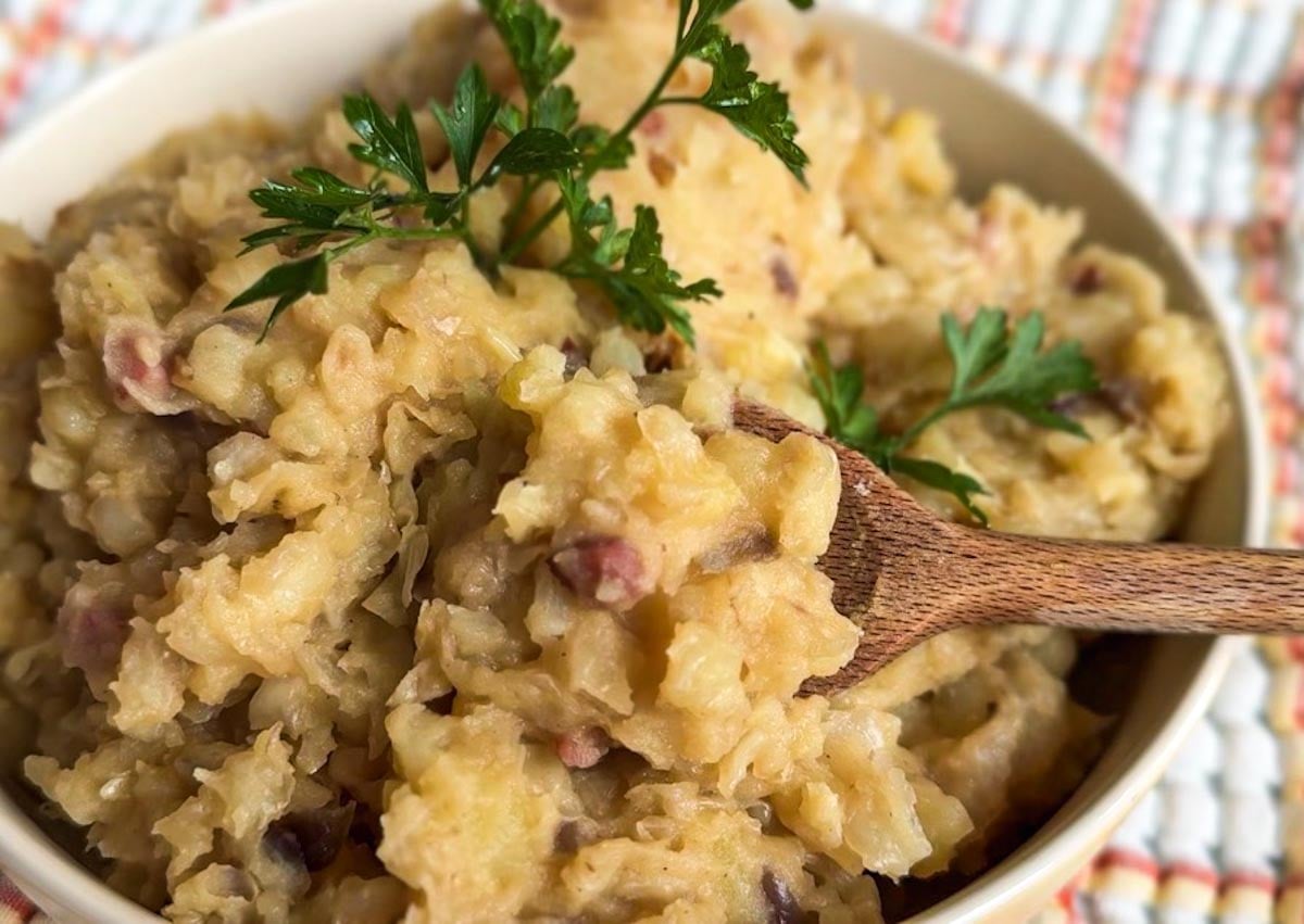 Creamy mashed potatoes with herbs and bacon bits in a bowl.