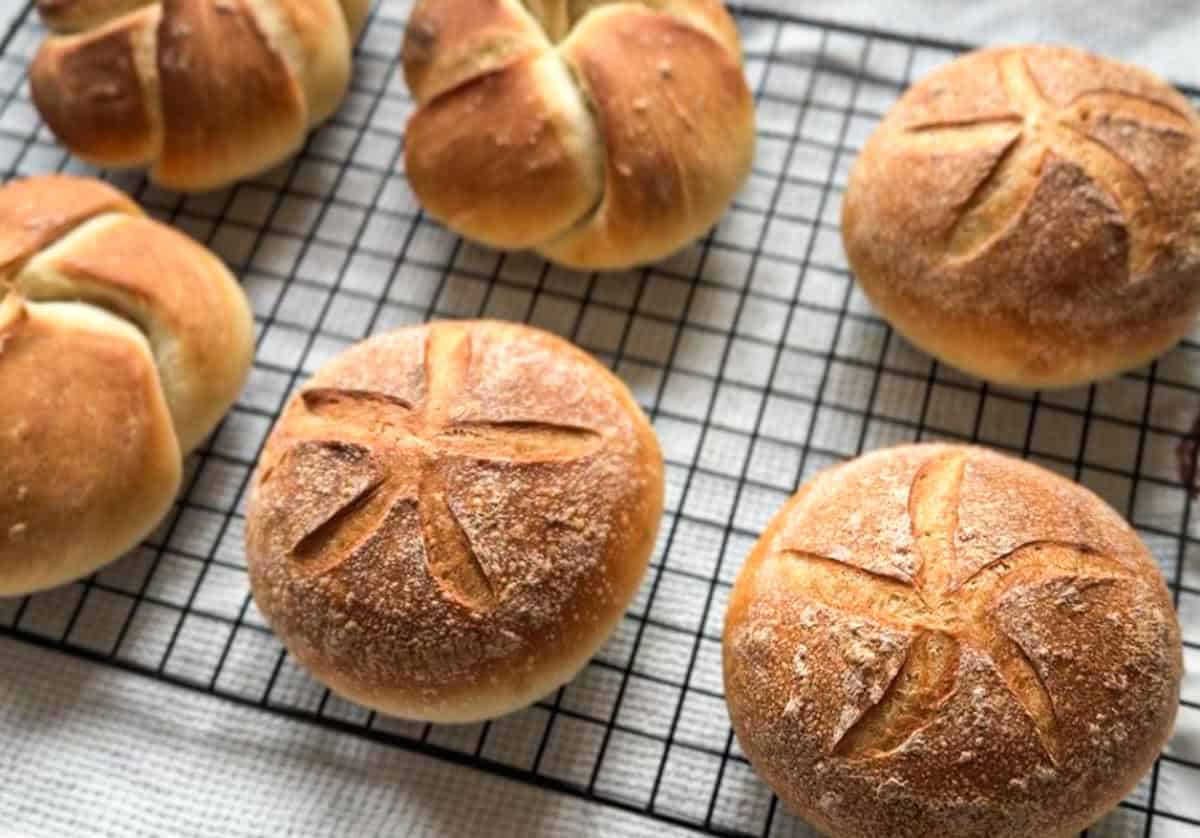 Fresh baked bread rolls on a cooling rack with scoring.