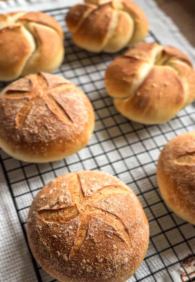 Scarred crust bread rolls cooling on a wire rack after baking.