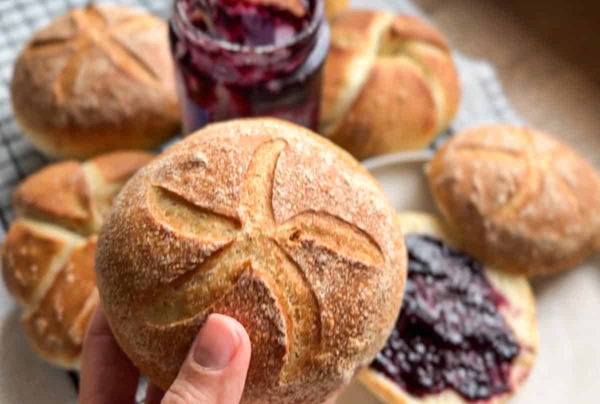 Close-up of hand holding round artisanal bread roll with scoring.