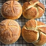 Stack of golden baked sourdough kaiser rolls on a cooling rack.