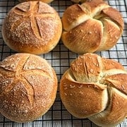 Fresh baked bread rolls with scoring on a cooling rack.
