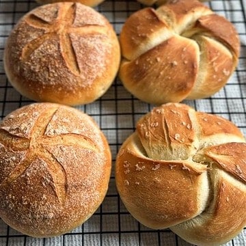 Fresh baked bread rolls with scoring on a cooling rack.