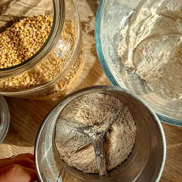 Close-up of freshly milled flour and grains in glass jars on a wooden surface.