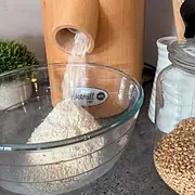 Wooden grain mill grinding flour into a glass bowl.