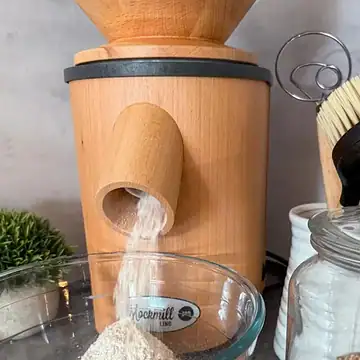 Wooden grain mill grinding flour into a glass bowl.