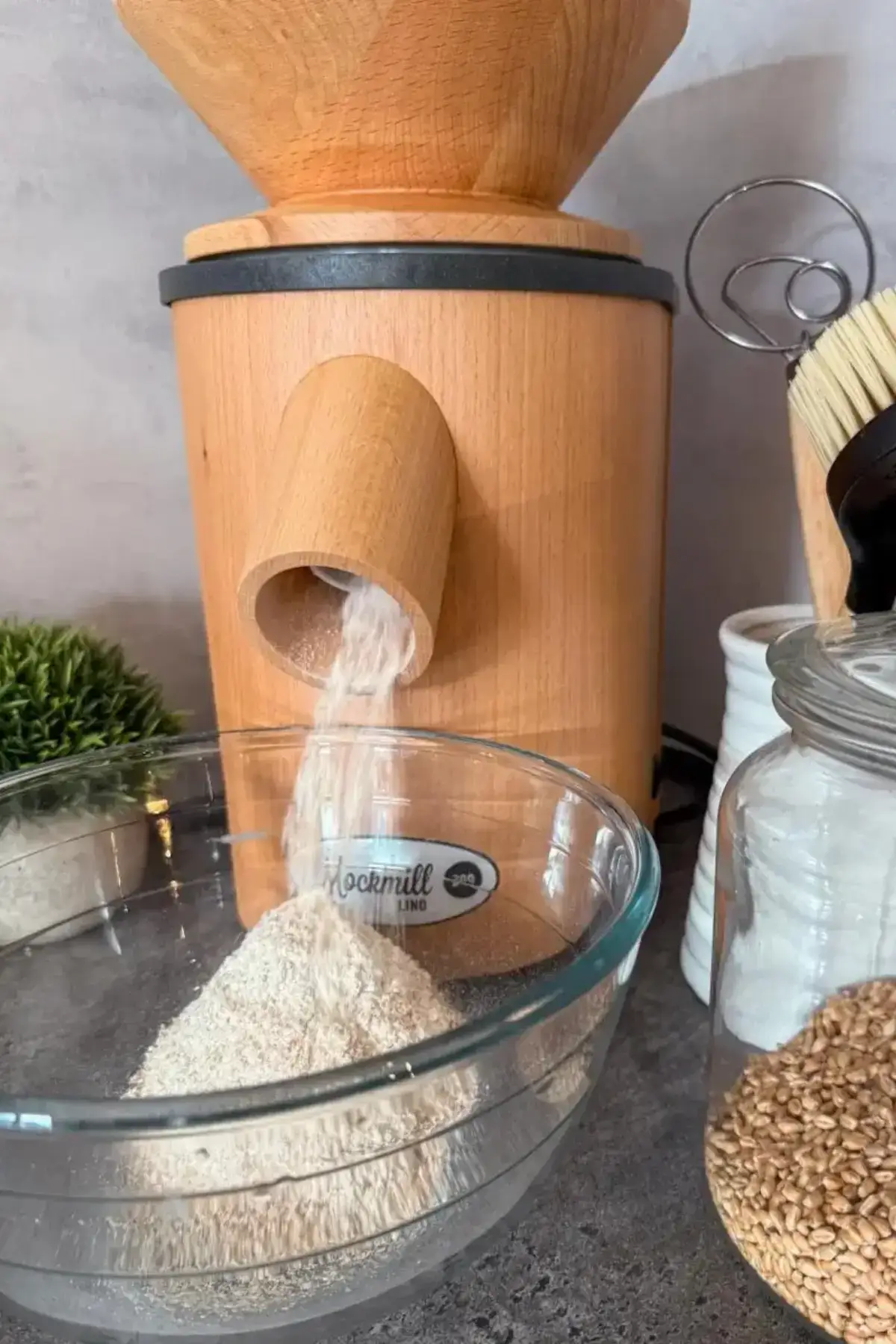 Wooden grain mill grinding flour into a glass bowl.