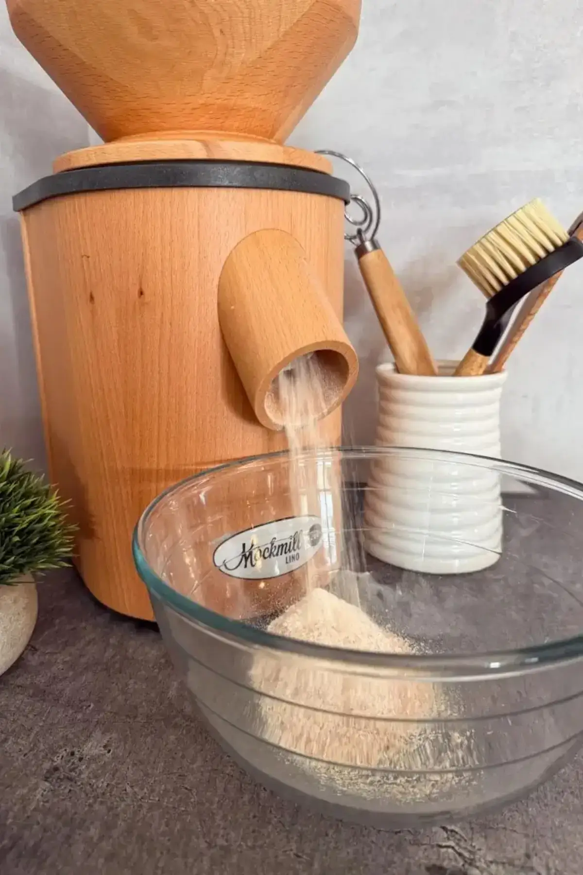 Wooden grain mill grinding flour into a glass bowl.