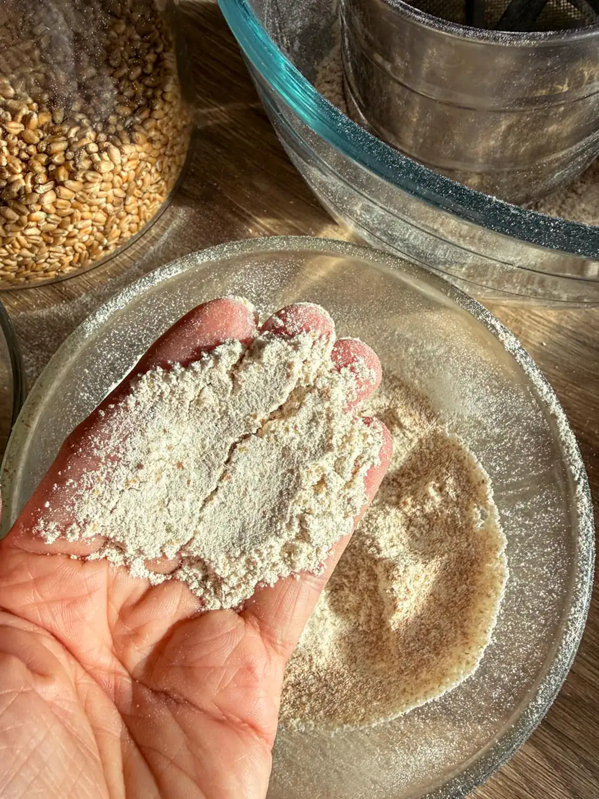 A handful of soft sifted fresh milled flour held over a glass bowl